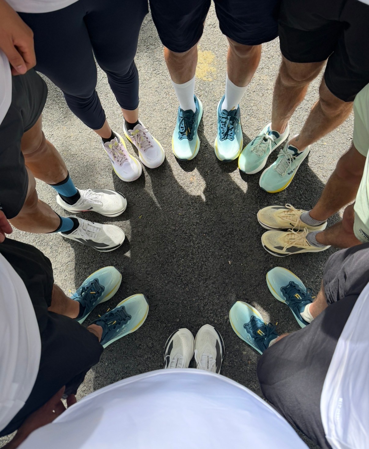 Grupo de corredoras y corredores en corro tras un entrenamiento, juntando sus zapatillas en el centro